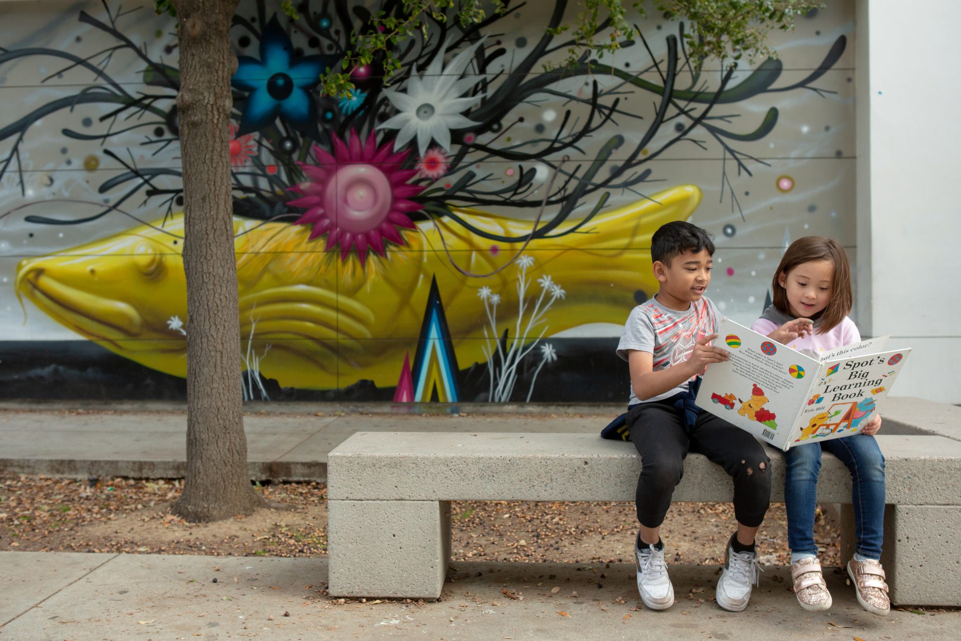 Two children sitting on a bench reading a book together