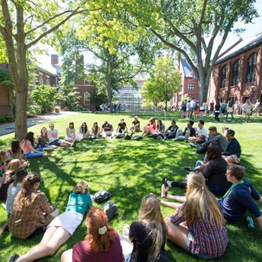 Kids sitting in a circle on the grass in the courtyard of a school.