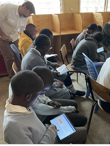 Photo of a roomful of students working on tablets with a teacher overseeing them.