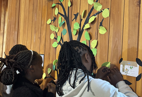 Photo of students writing notes on a paper leaves to add to a paper tree