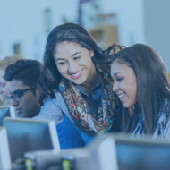 Teacher looking over students shoulder as she works on a computer, both smiling